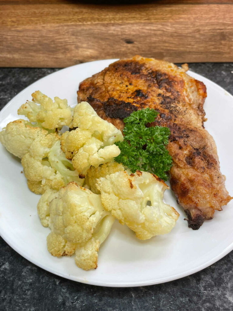 Roasted Cauliflower on a white plate with a pork chop